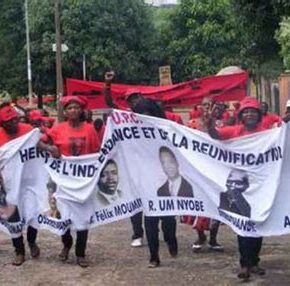 Manifestation de l'Union des peuples du Cameroun avec une banderole où il y a les visages des différents militant·e·s de l'UPC.